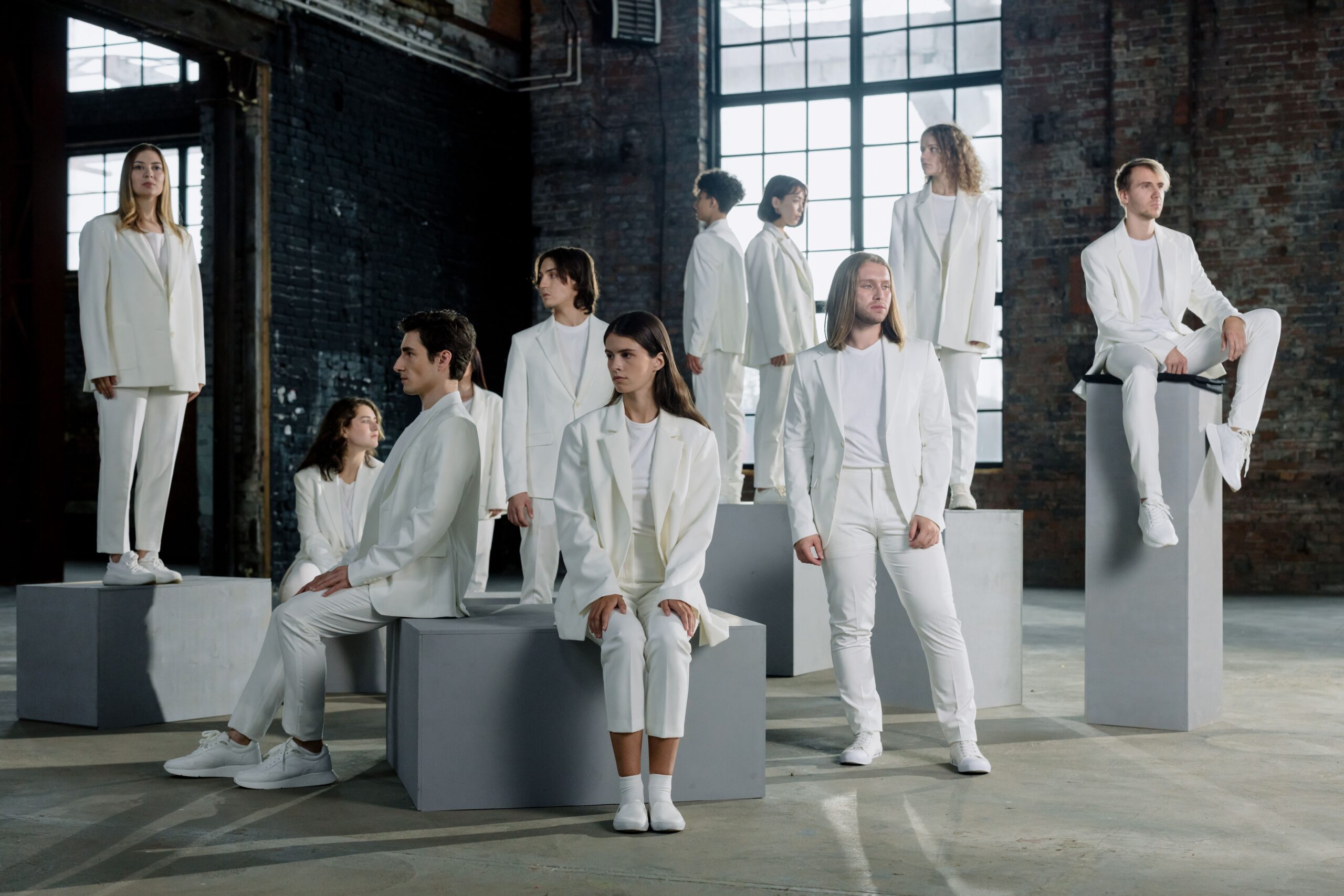 Diverse group of individuals in white clothing posing on platforms indoors with natural lighting.
