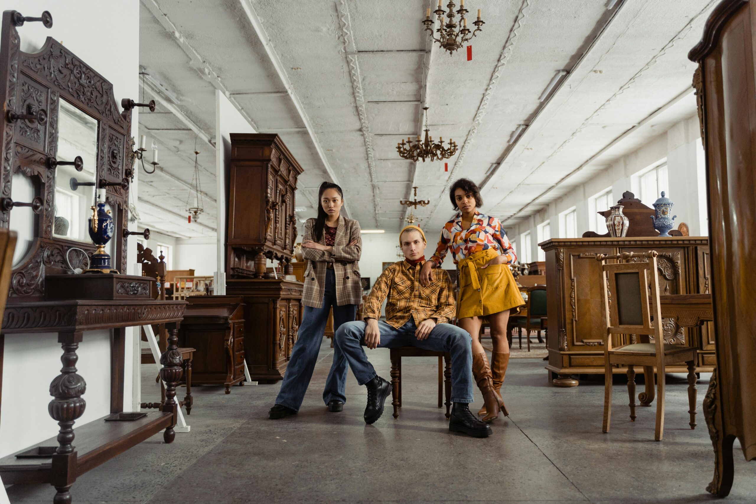 Stylish young adults posing amidst vintage furniture in a spacious warehouse setting.